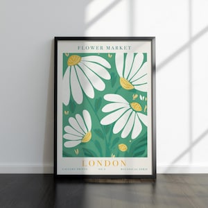 May include: A framed art print with a floral design. The artwork features large white daisies with yellow centres set against a green backdrop. The text "FLOWER MARKET LONDON" is displayed at the top and bottom of the print.