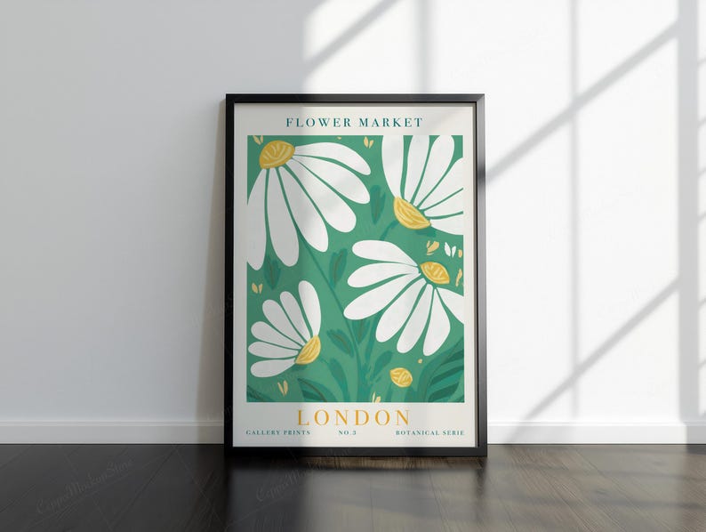 May include: A framed art print with a floral design. The artwork features large white daisies with yellow centres set against a green backdrop. The text "FLOWER MARKET LONDON" is displayed at the top and bottom of the print.