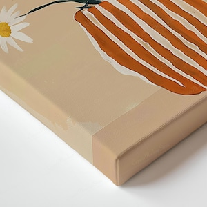 May include: A canvas print depicting a daisy and a vase with orange and white stripes. The artwork has a neutral colour palette with a beige background and a white border.
