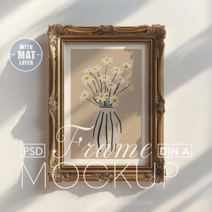 Puede incluir: Un marco dorado adornado con un paspartú blanco y una impresión de un ramo de margaritas blancas en un jarrón. El marco está en una pared blanca con sombras de la luz del sol.