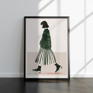 May include: A framed art print showing a minimalist illustration of a person walking. The figure is wearing a green sweater and a striped skirt, with black shoes. The artwork is set against a neutral background.