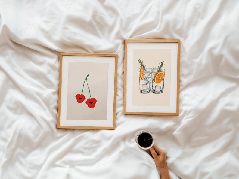 Puede incluir: Dos impresiones art&iacute;sticas enmarcadas con marcos de madera. Una impresi&oacute;n presenta labios rojos como cerezas, la otra muestra dos vasos de c&oacute;ctel con hielo, rodajas de naranja y romero. Una taza de caf&eacute; se sostiene en la mano.