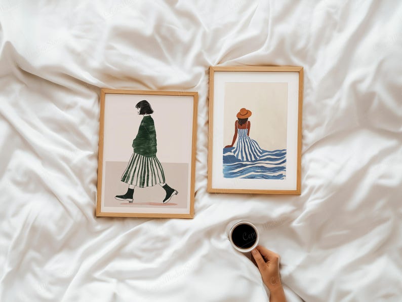 Puede incluir: Dos impresiones art&iacute;sticas enmarcadas sobre una superficie blanca. Una impresi&oacute;n representa a una persona con un su&eacute;ter verde y una falda a rayas caminando. La otra muestra a una persona con un vestido a rayas y un sombrero sentada cerca del agua azul. Una mano sostiene una taza de caf&eacute;.