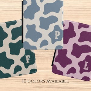 May include: A collection of three cases with a cow print design in various colors: teal, blue, and purple. Each case features a different initial: F, P, and L. The text "10 COLORS AVAILABLE" is displayed at the bottom.