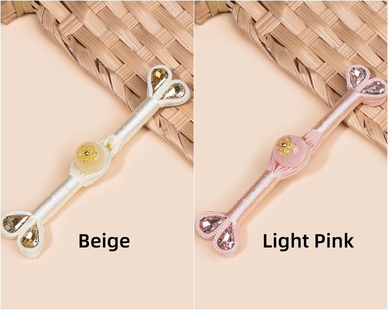 Op de afbeelding: Twee decoratieve haaraccessoires, &eacute;&eacute;n beige en &eacute;&eacute;n lichtroze, elk met een centrale bloemenversiering en hartvormige kristallen accenten. Het beige accessoire heeft goudkleurige kristallen, het roze heeft roze kristallen.
