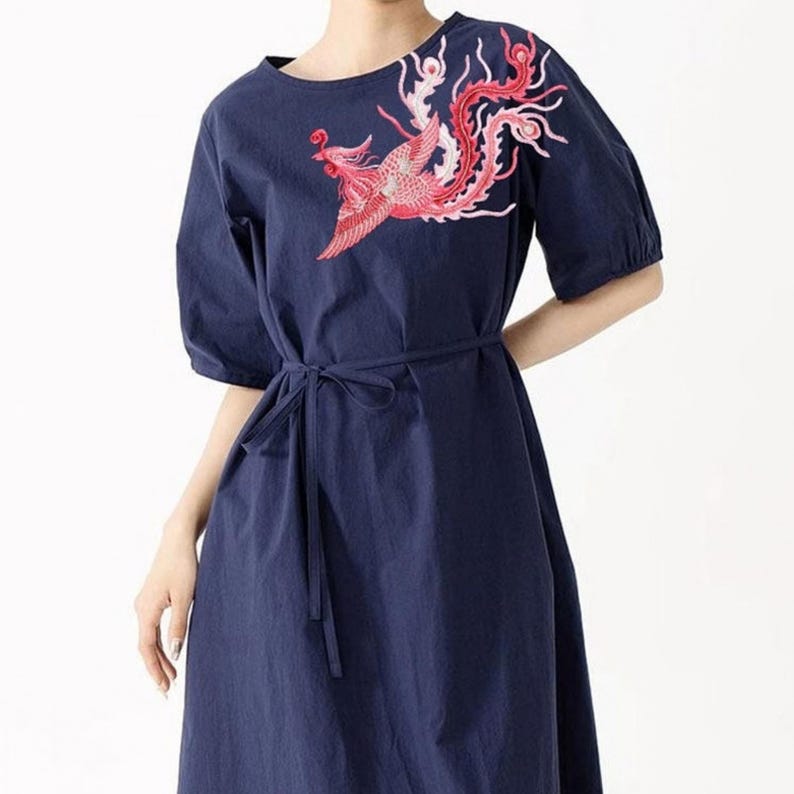 Puede incluir: Vestido azul marino con cuello redondo y mangas cortas. El vestido presenta una cintura anudada y un dise&ntilde;o de f&eacute;nix bordado en rojo y rosa en la parte superior izquierda. Una prenda elegante y c&oacute;moda.