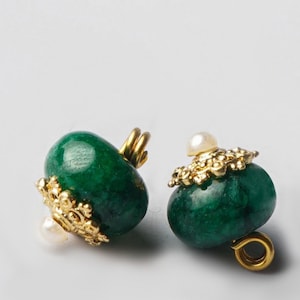 May include: Two green stone earrings with gold-colored accents. Each earring features a polished, oval-shaped green stone, adorned with a gold-colored filigree and a small, white pearl. The earrings have a post and loop design.