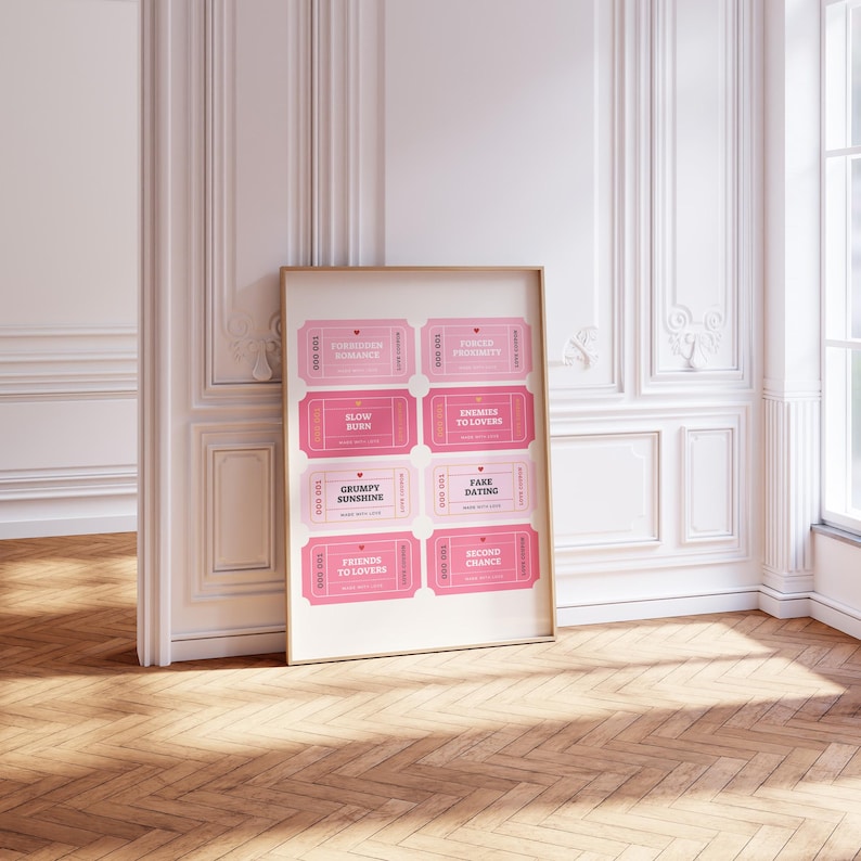 May include: A framed print featuring eight pink ticket designs with phrases like "Forbidden Romance" and "Fake Dating." The tickets have a vintage aesthetic with a light pink background and darker pink text. The print is displayed against a white wall.