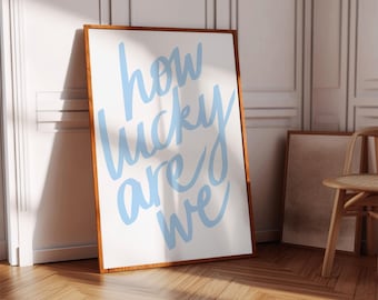 May include: A framed print with a white background and a light blue inscription that reads "how lucky are we".