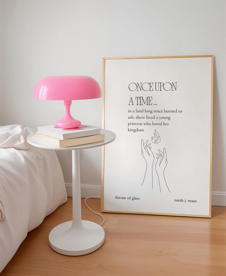 K&ouml;nnte beinhalten: Eine pinkfarbene Pilzlampe steht auf einem wei&szlig;en Beistelltisch mit B&uuml;chern. Ein gerahmter Druck mit dem Text "ONCE UPON A TIME..." und "throne of glass" lehnt an der Wand. Der Raum hat einen minimalistischen Stil.