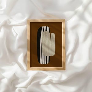 May include: A rectangular wooden frame containing a print with a solid dark brown background. The central graphic features a vertical black shape with white stripes, partially overlaid by a textured, light beige, U-shaped form.