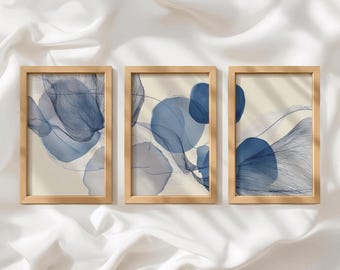 Può includere: Un set di tre stampe artistiche rettangolari con cornici in legno chiaro. Ogni stampa presenta forme circolari blu astratte e sottili linee blu scuro sovrapposte a uno sfondo color crema, creando una serie visiva coerente e uniforme.
