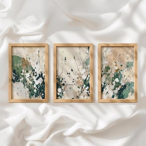 Puede incluir: Un conjunto de tres cuadros rectangulares con marcos de madera clara. Cada lámina presenta una composición abstracta con salpicaduras y pinceladas en tonos verde salvia, verde bosque oscuro, crema y beige, creando un efecto botánico.