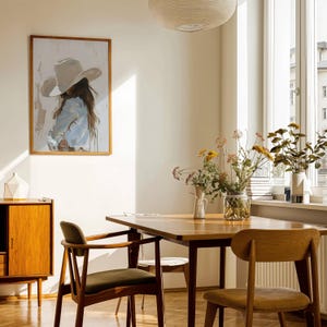 Pode incluir: Uma sala de jantar com uma mesa e cadeiras de madeira, um arm&aacute;rio de madeira e uma obra de arte emoldurada. A obra retrata uma pessoa com um chap&eacute;u de cowboy. Vasos de flores est&atilde;o sobre a mesa e a janela. O quarto tem uma atmosfera acolhedora.