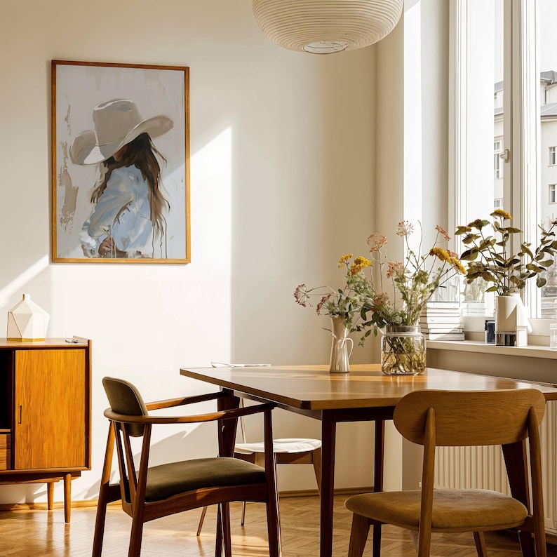 Pode incluir: Uma sala de jantar com uma mesa e cadeiras de madeira, um arm&aacute;rio de madeira e uma obra de arte emoldurada. A obra retrata uma pessoa com um chap&eacute;u de cowboy. Vasos de flores est&atilde;o sobre a mesa e a janela. O quarto tem uma atmosfera acolhedora.