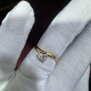 Peut inclure: Une bague en or avec un pendentif en forme de cœur serti de diamants. La monture de la bague est en or poli, et le pendentif en forme de cœur est orné de petits diamants. La bague est présentée sur un gant blanc.