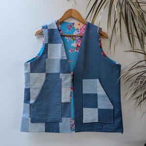 Puede incluir: Un chaleco reversible sin mangas con un exterior de mezclilla de retazos con paneles cuadrados alternos en azul claro y oscuro y dos bolsillos delanteros. El interior está forrado con una tela azul brillante con un estampado floral rosa y blanco.