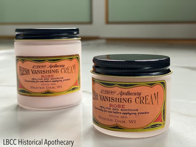 May include: Two small jars of LBCC Apothecary Flesh Vanishing Cream, with black lids and labels featuring text. The labels read "Rose Healing and Soothing" and "Beaver Dam, WI". The jars are on a white surface.