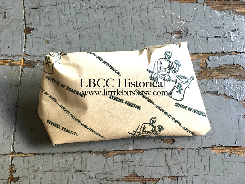 Puede incluir: Un paquete envuelto en papel marr&oacute;n con ilustraciones verdes y texto, incluyendo "Ciencia de la farmacia" y "Pr&aacute;ctica &eacute;tica". El paquete est&aacute; sobre una superficie gris desgastada. El texto "LBCC Historical" y una direcci&oacute;n web tambi&eacute;n son visibles.