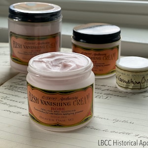 May include: Several jars of LBCC Apothecary "Flesh Vanishing Cream" with rose scent. The jars are white with black lids and labels with text. The cream is pink and the labels have a vintage design.
