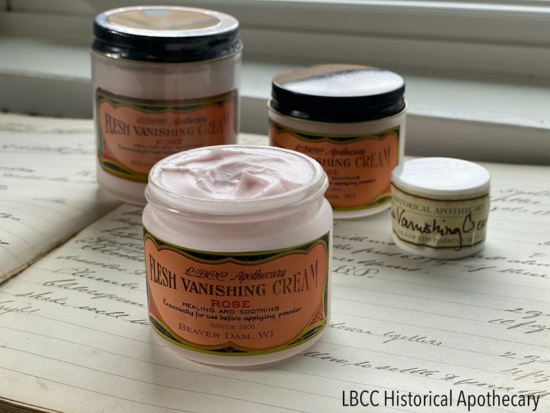 May include: Several jars of LBCC Apothecary "Flesh Vanishing Cream" with rose scent. The jars are white with black lids and labels with text. The cream is pink and the labels have a vintage design.