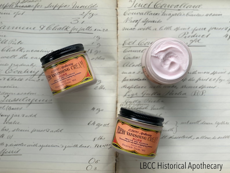 May include: Three jars of LBCC Apothecary Flesh Vanishing Cream with Rose, a healing and soothing cream. The jars have black lids and labels with text. The cream is pink and sits on a vintage ledger.