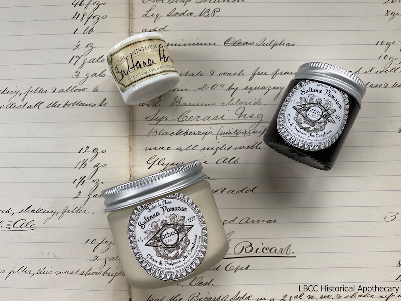 May include: Three small jars of cream or balm with silver lids. The jars are labeled "Sultana Pomatum" and "Sultana Balm" with the text "Apothecary London" on the labels. The jars are sitting on a page of a notebook with handwritten text.