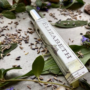 May include: A silver and white bottle of perfume with the word "Elizabeth" printed on the label. The bottle is surrounded by green leaves and lavender flowers.
