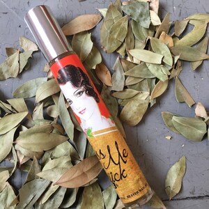 Peut inclure: Un petit flacon en verre transparent avec un bouchon argent&eacute;. Le flacon porte une &eacute;tiquette rouge, orange et jaune avec une illustration vintage d'une femme et le texte "Kiss Me Quick".
