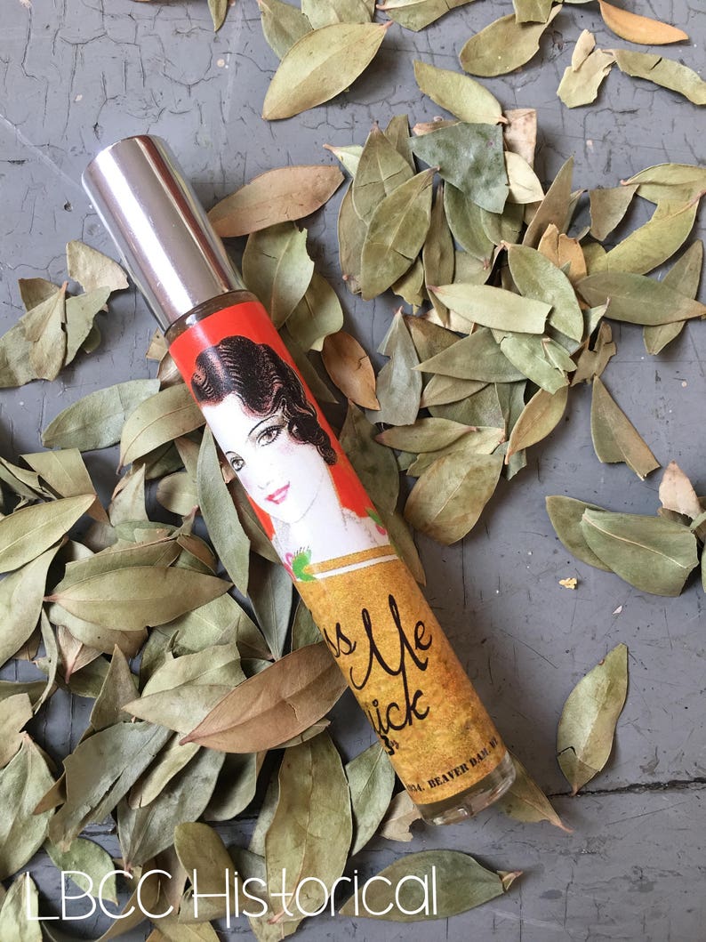 Peut inclure: Un petit flacon en verre transparent avec un bouchon argent&eacute;. Le flacon porte une &eacute;tiquette rouge, orange et jaune avec une illustration vintage d'une femme et le texte "Kiss Me Quick".