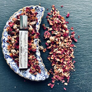 K&ouml;nnte beinhalten: Eine Glasflasche mit Parf&uuml;m, einem silbernen Verschluss und einem wei&szlig;en Etikett mit der Aufschrift "Bouquet de l'Imp&eacute;ratrice". Die Flasche steht auf einer blauen und wei&szlig;en Porzellanschale mit getrockneten Rosenbl&auml;ttern. Die Schale ist halbmondf&ouml;rmig. Getrocknete Rosenbl&auml;tter sind um die Schale herum verstreut.