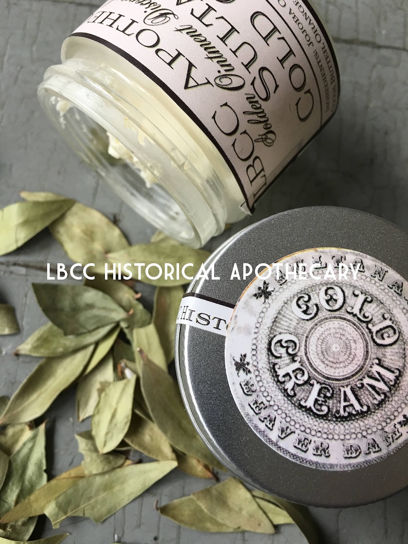 K&ouml;nnte beinhalten: Ein kleines Glasgef&auml;&szlig; mit einem wei&szlig;en Etikett, auf dem "LBCC Apothecary Golden Ointment Cold Soothing" steht, und eine silberne Metalldose mit einem wei&szlig;en Etikett, auf dem "LBCC Historical Apothecary Cold Cream Beaver Dam" steht.
