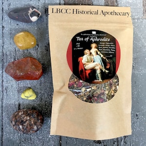 May include: A brown paper bag with a clear window showing a blend of dried herbs and flowers. The bag is labeled "LBCC Historical Apothecary" and "Tea of Aphrodite". The label also lists the ingredients: Orange, Peppermint, Lavender, Ginger, Clove, Rose, Rosemary, Thyme, Cinnamon, Hibiscus.