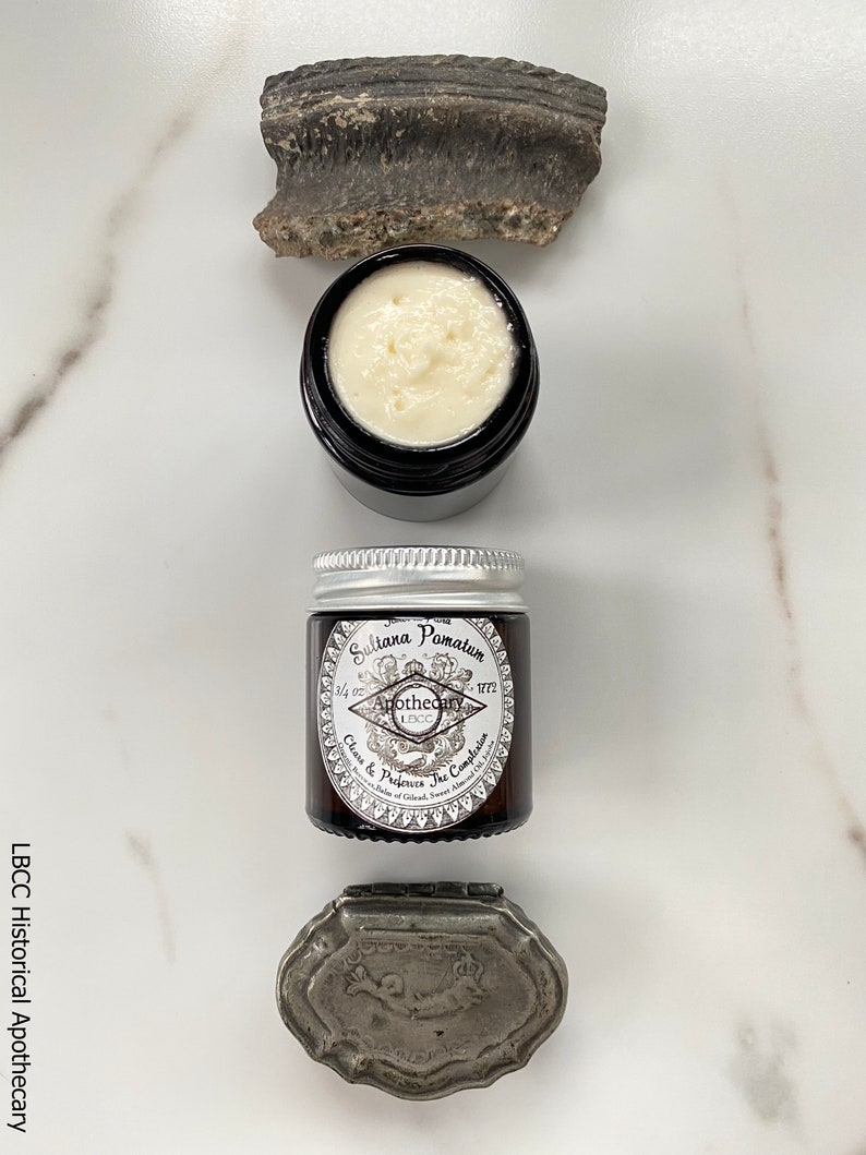 May include: A small glass jar with a silver lid containing Sultana Pomatum, a cream to cleanse and preserve the complexion. The jar has a label with the text "Sultana Pomatum", "Apothecary 1772", and "Cleanse & Preserve the Complexion".
