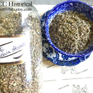 Puede incluir: Un gran tarro de vidrio lleno de salvia seca, etiquetado como "SAGE Salvia officinalis". Un cuenco azul y blanco con dibujos contiene m&aacute;s salvia. La imagen tambi&eacute;n muestra un plato estampado y el texto "LBCC Historical" y "www.littlebits.etsy.com."