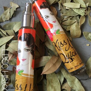Peut inclure: Deux petits flacons en verre avec un design vintage. Les flacons sont remplis d'un liquide clair et ont un embout pulv&eacute;risateur. Les flacons ont un fond jaune avec une illustration rouge et orange d'une femme et le texte "Kiss Me Quick".