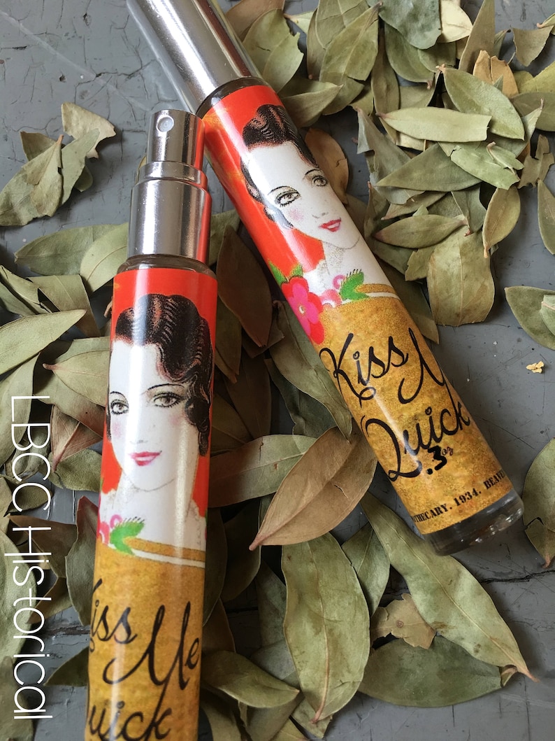 Peut inclure: Deux petits flacons en verre avec un design vintage. Les flacons sont remplis d'un liquide clair et ont un embout pulv&eacute;risateur. Les flacons ont un fond jaune avec une illustration rouge et orange d'une femme et le texte "Kiss Me Quick".