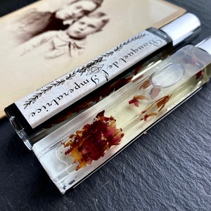 K&ouml;nnte beinhalten: Zwei durchsichtige Glasflaschen mit silbernen Kappen, gef&uuml;llt mit einer klaren Fl&uuml;ssigkeit und getrockneten Blumen. Das Etikett auf einer Flasche lautet "Journal of Imperfections" und "Boundless"