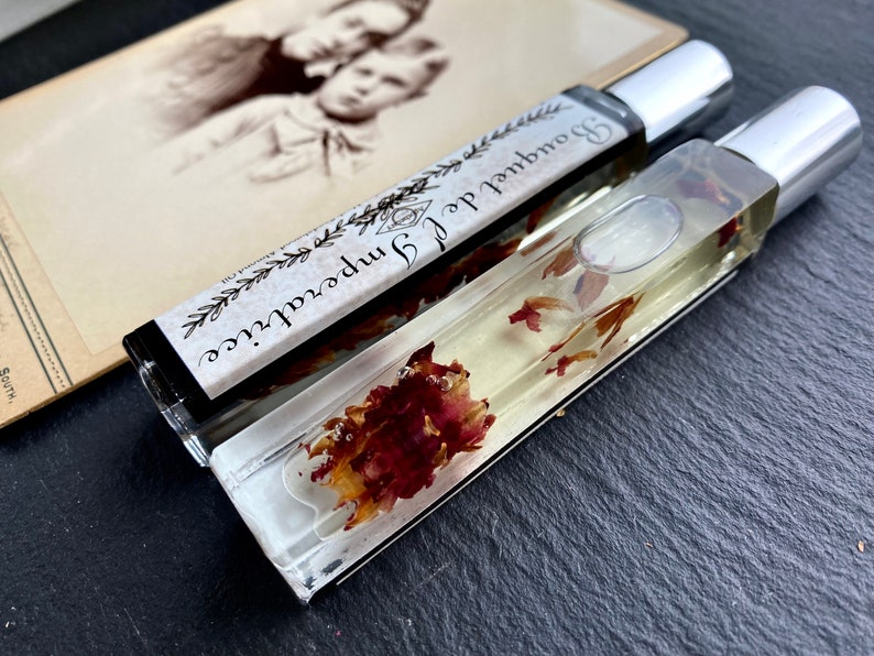 K&ouml;nnte beinhalten: Zwei durchsichtige Glasflaschen mit silbernen Kappen, gef&uuml;llt mit einer klaren Fl&uuml;ssigkeit und getrockneten Blumen. Das Etikett auf einer Flasche lautet "Journal of Imperfections" und "Boundless"