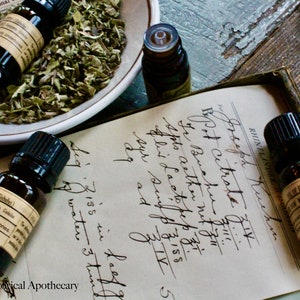 May include: Four small brown glass bottles with black caps containing essential oils. The bottles are sitting on a vintage notebook with handwritten text. The text includes the words "Bpot citrate" and "Buchu".