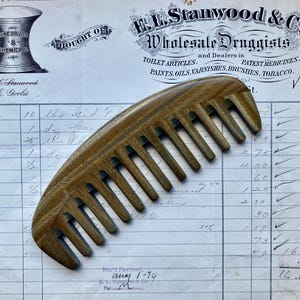 May include: A wooden comb with a brown and tan color. The comb is lying on a piece of paper with handwritten text. The text includes the words "E.L. Stanwood & Co. Wholesale Druggists" and "Rec'd Payment, May 1-74".