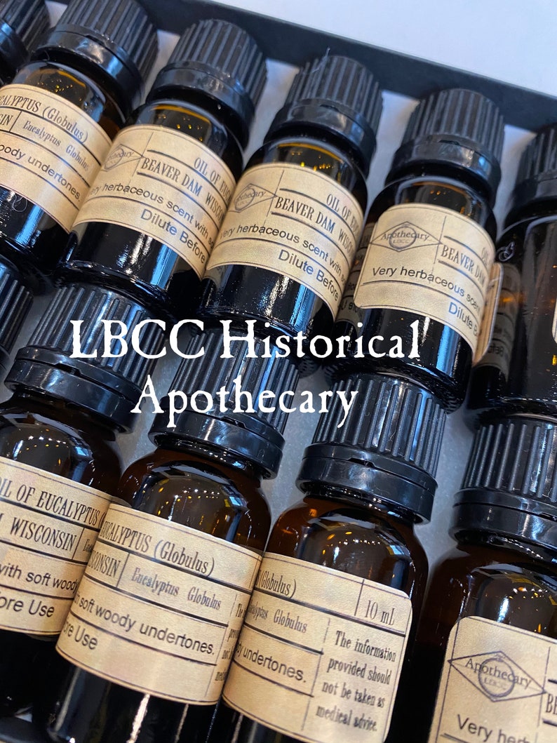 May include: A collection of small amber glass bottles with black caps, labeled with the text "LBCC Historical Apothecary". The bottles contain essential oils, including "Oil of Eucalyptus (Globulus)" and "Beaver Dam Wisconsin".