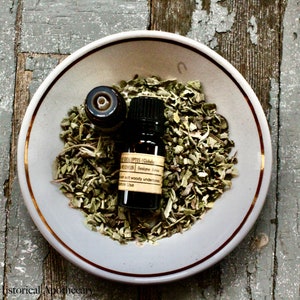 May include: A small dark brown glass bottle with a gold label that reads "EUCALYPTUS GLOBULUS" and "Botanical Essence" on a white plate with dried green herbs.