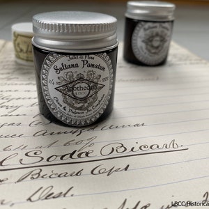 May include: A small, black jar with a silver lid. The jar is labeled "Joilet de Flora Sultana Pomatum 3/4 oz Apothecary 18CC Clears & Perfects The Complexion"