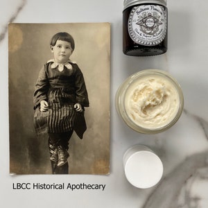 May include: A vintage postcard featuring a black and white photo of a young girl wearing a dark dress and shoes. The postcard is labeled "LBCC Historical Apothecary".  There are three jars of cream, one with a silver lid and the label "Sulitana Pomatia Cream & Perfume, The Complexion"