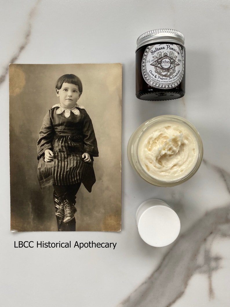 May include: A vintage postcard featuring a black and white photo of a young girl wearing a dark dress and shoes. The postcard is labeled "LBCC Historical Apothecary".  There are three jars of cream, one with a silver lid and the label "Sulitana Pomatia Cream & Perfume, The Complexion"