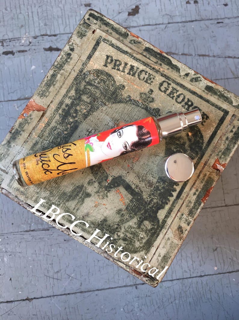 Peut inclure: Un flacon de parfum de style vintage avec une &eacute;tiquette rouge, blanche et jaune qui indique "It's all juice". Le flacon est pos&eacute; sur une bo&icirc;te en bois avec les mots "Prince George" et "LBCC Historical" imprim&eacute;s dessus.