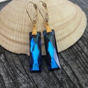 May include: A pair of gold dangle earrings with blue crystal teardrop-shaped pendants.