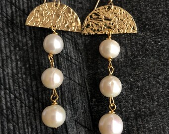 Peut inclure: Boucles d'oreilles en or avec un design en demi-cercle martelé et trois perles blanches suspendues à chaque boucle d'oreille.