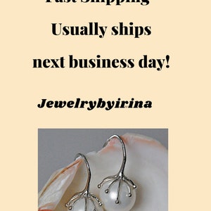 Op de afbeelding: Een paar zilverkleurige oorbellen met ronde witte parels die worden vastgehouden door een klauwachtige zetting. De oorbellen worden getoond tegen een lichte schelp. De tekst luidt: Fast Shipping- Usually ships next business day! Jewelrybyirina.